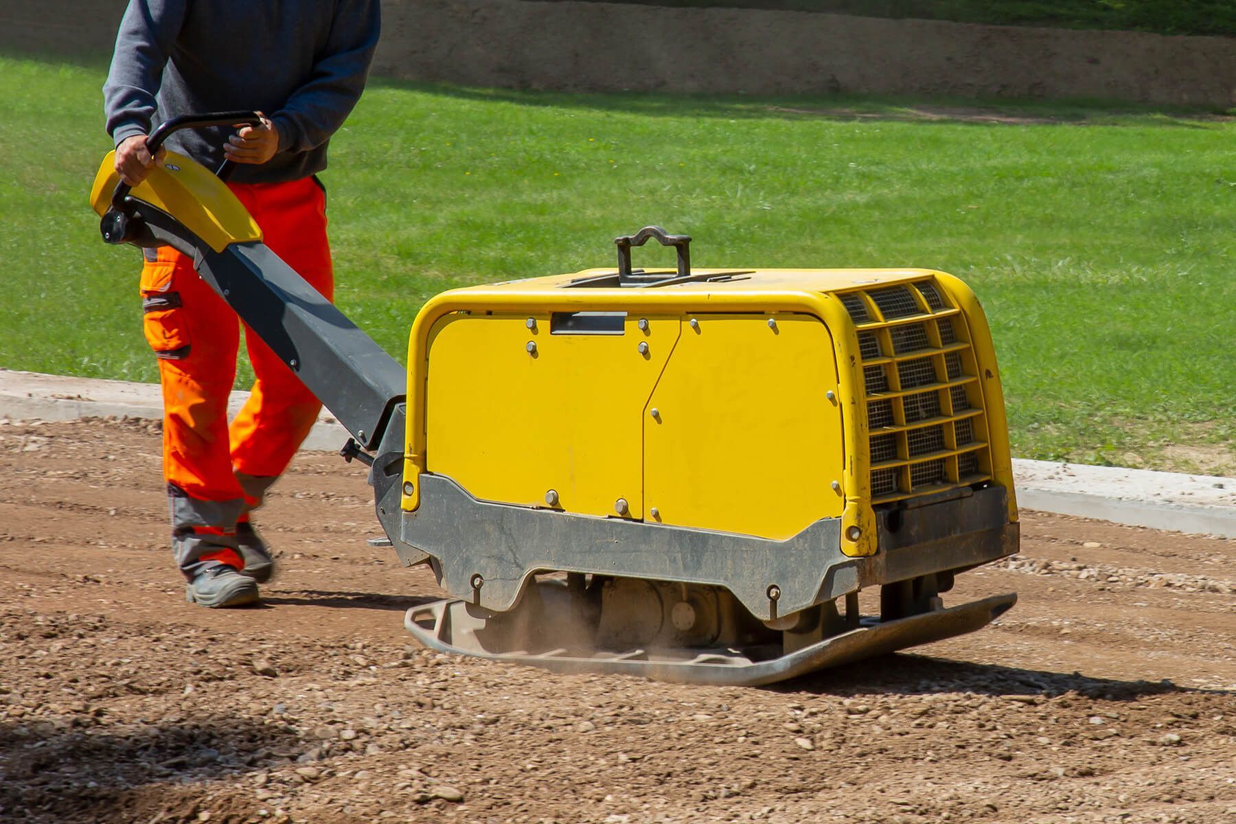 a man is using a yellow machine to compact dirt .