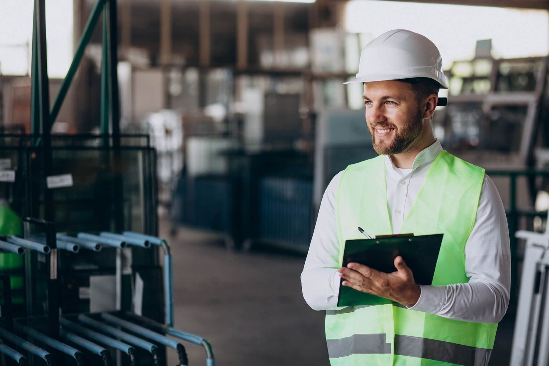 a man in a hard hat and safety vest is holding a clipboard in a factory .