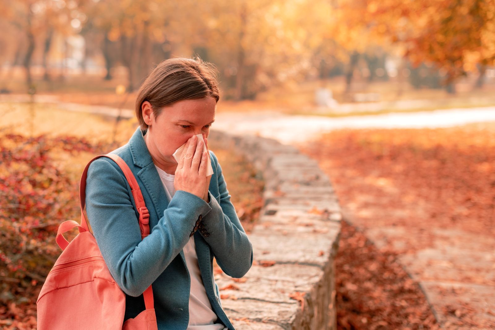 Person with backpack covers face beside a stone path in an autumn park