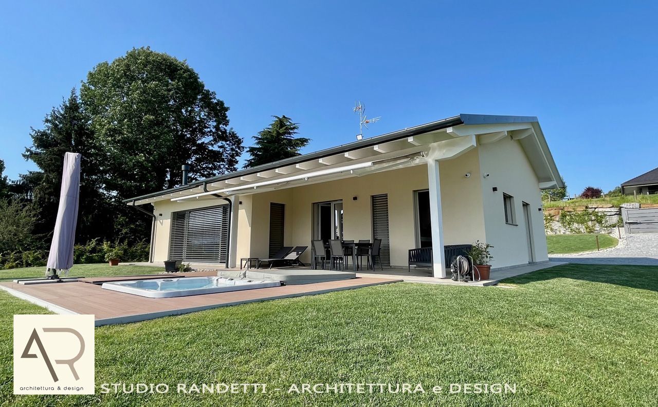 Casa bianca a un solo piano con patio coperto, prato e cielo azzurro.
