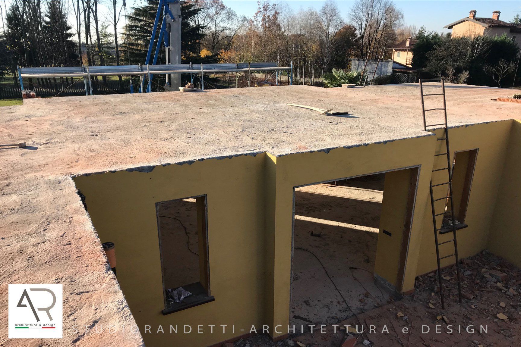 Struttura in cemento giallo con porta aperta e scala su un tetto piano in costruzione