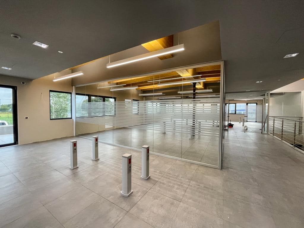 Atrio moderno e vuoto con pareti in vetro, pavimento piastrellato e tornelli metallici all'ingresso.