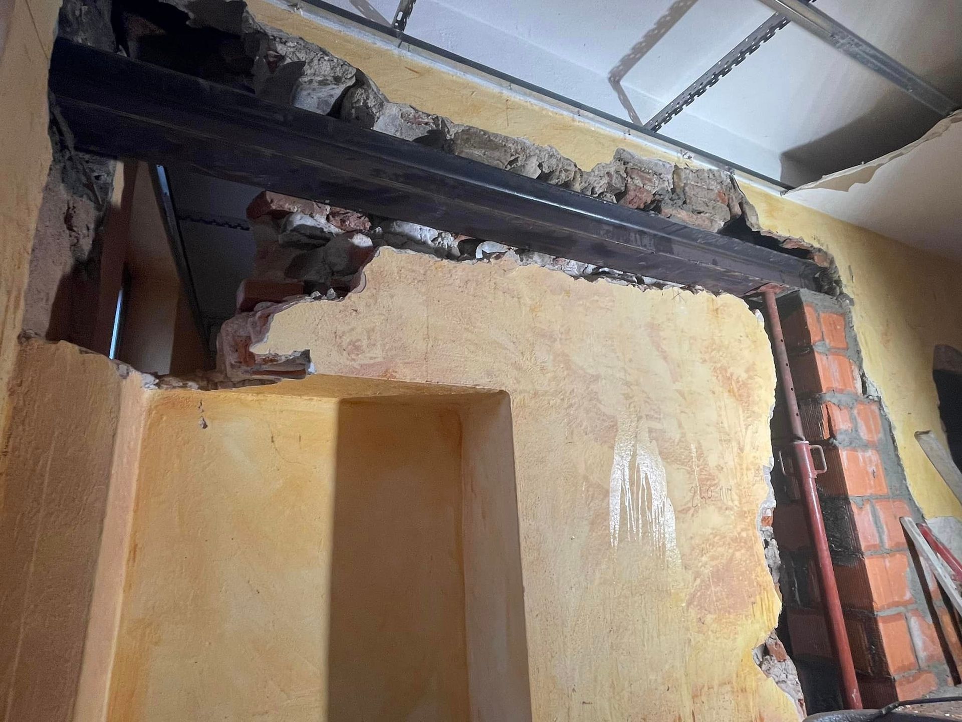 Soffitto interno danneggiato con travi a vista e intonaco screpolato vicino a un muro di mattoni.