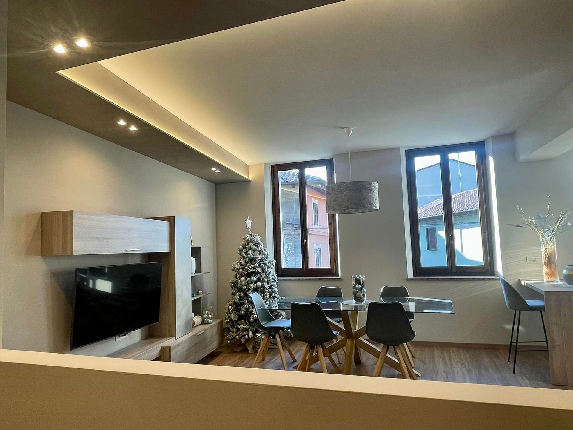 Soggiorno-sala da pranzo moderno con camino, albero di Natale e ampie finestre che lasciano entrare la luce naturale.
