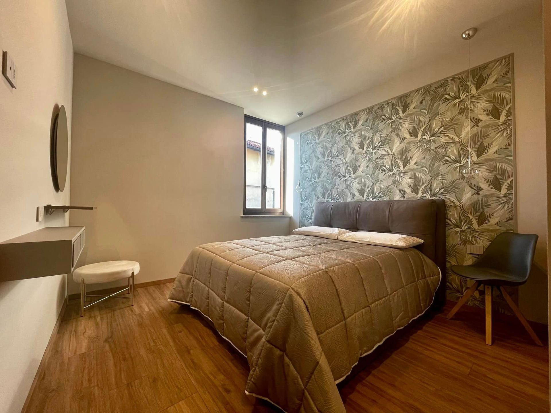 Camera da letto moderna con letto, parete decorativa con motivo, pavimento in legno e finestra che lascia entrare la luce.