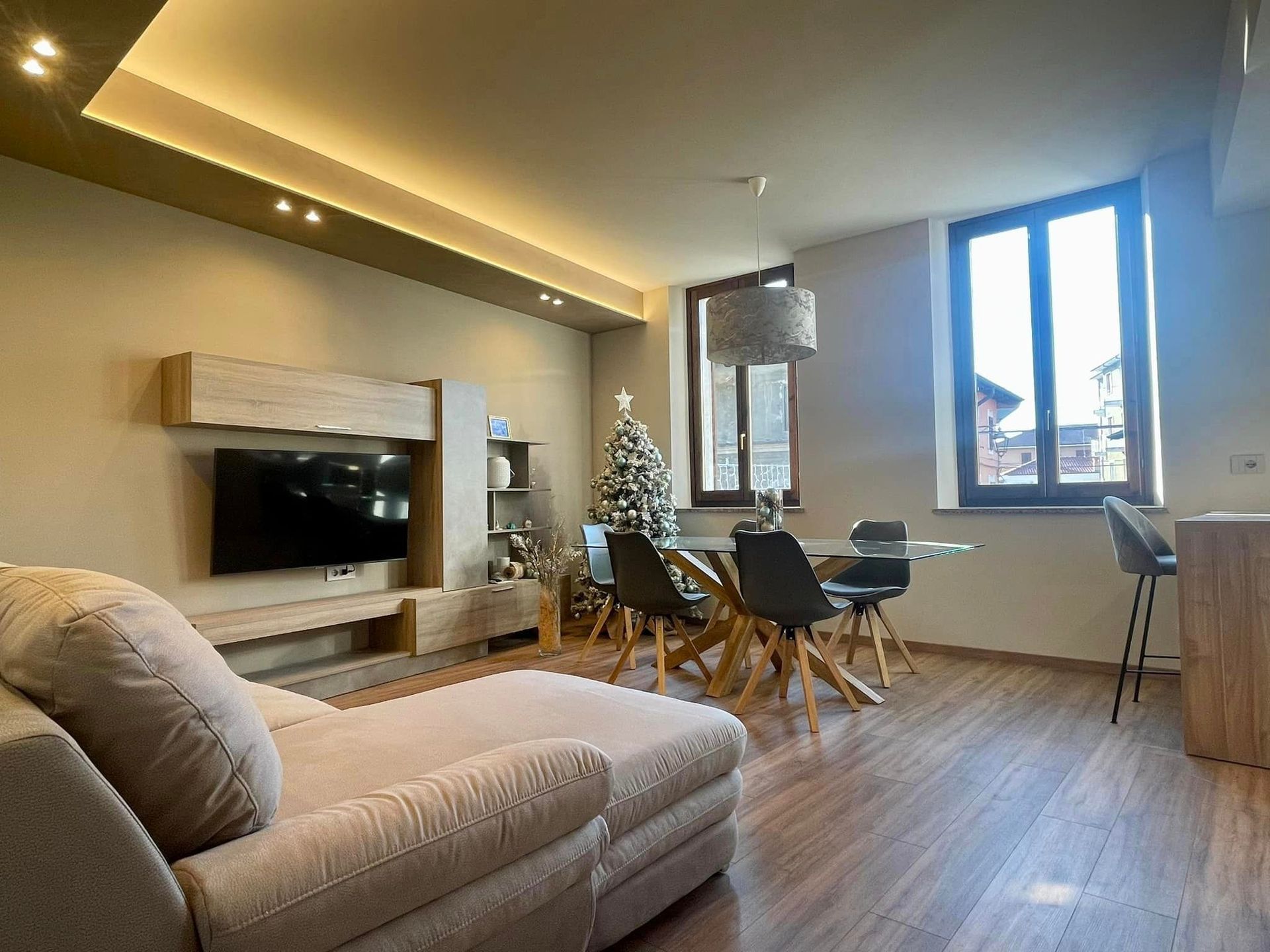Soggiorno moderno con divano angolare beige, camino, tavolo da pranzo e ampia finestra con vista sulla città.