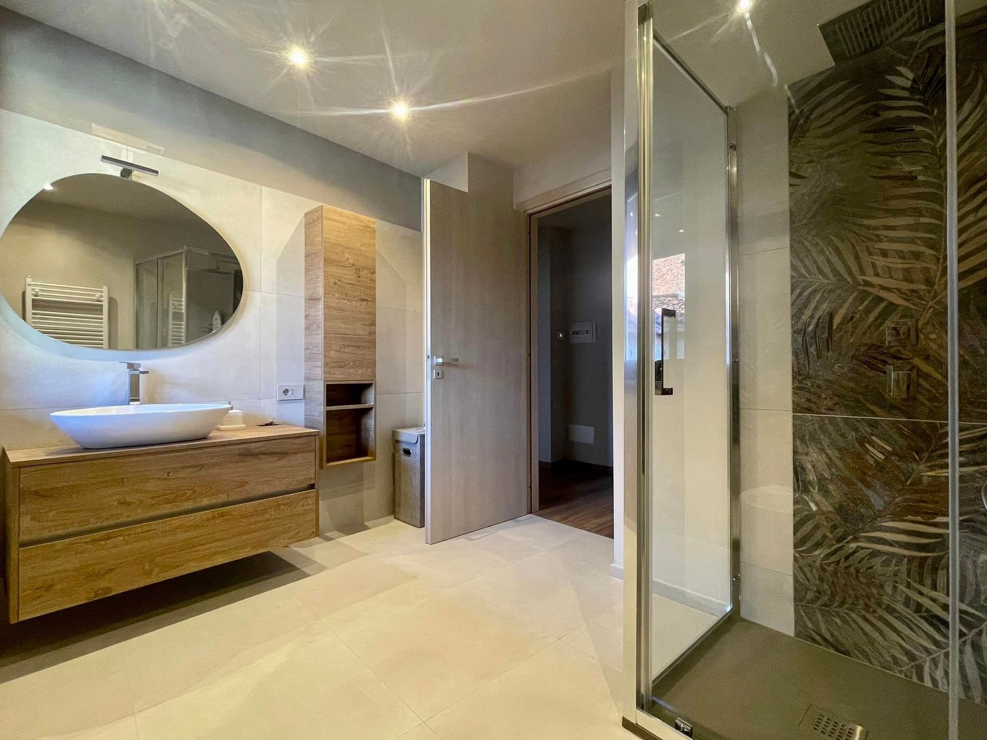 Bagno moderno con mobile lavabo in legno, specchio rotondo e box doccia in vetro.