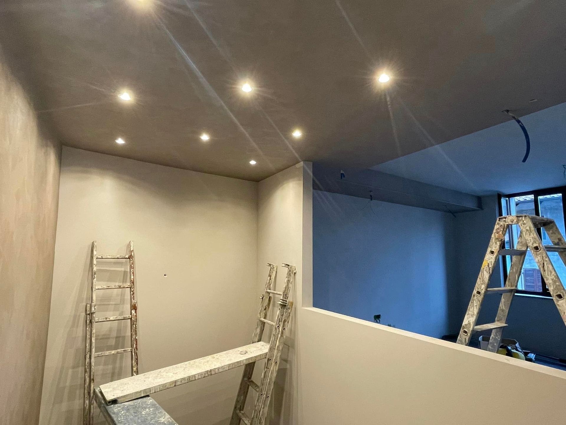 Stanza in fase di ristrutturazione con faretti a incasso a soffitto, scale e una parete divisoria parzialmente costruita.