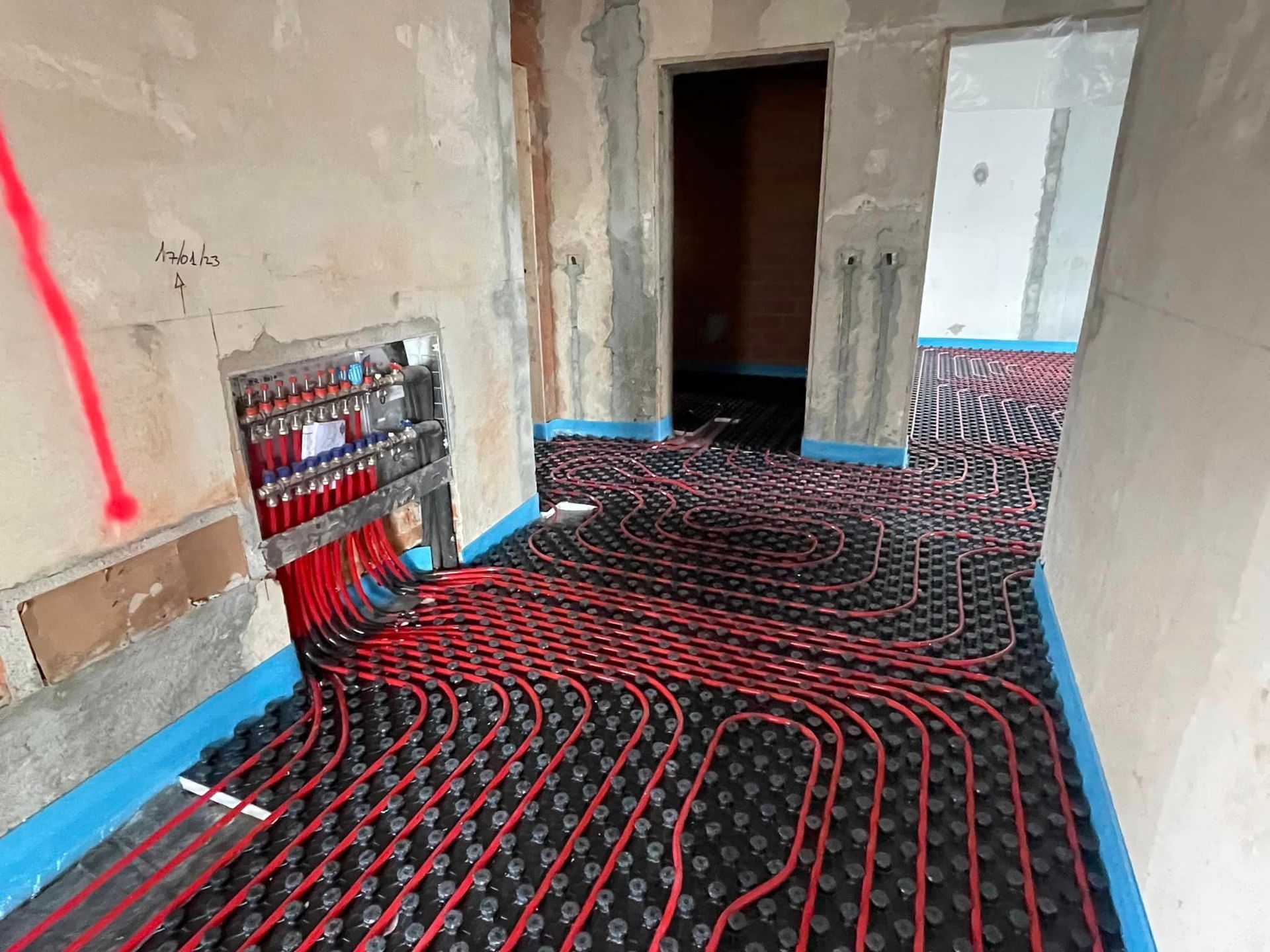 Corridoio interno con tubi rossi per il riscaldamento a pavimento installati sopra l'isolamento nero e pareti a vista.