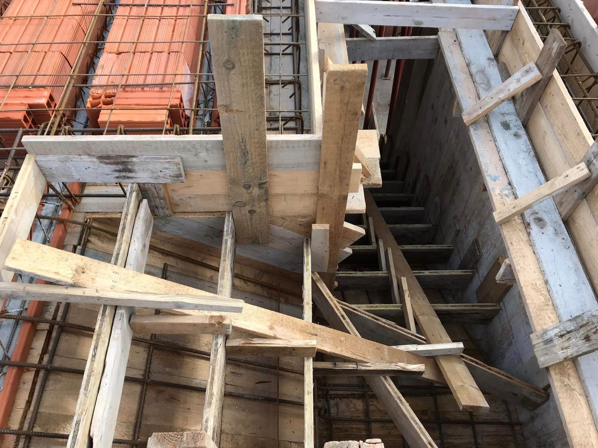 Cantiere edile con casseforme in legno e colonne in cemento armato attorno a un pozzo aperto.