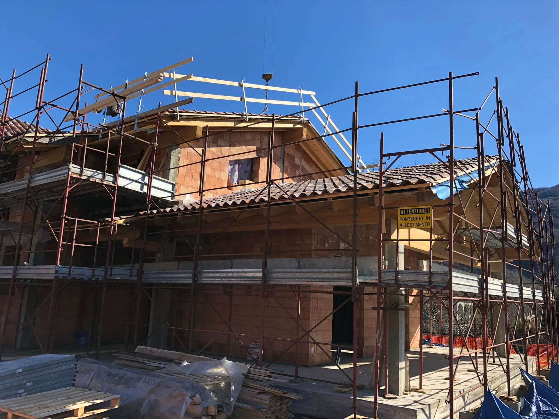 Casa in costruzione con impalcature e struttura a vista sullo sfondo di un cielo azzurro limpido.