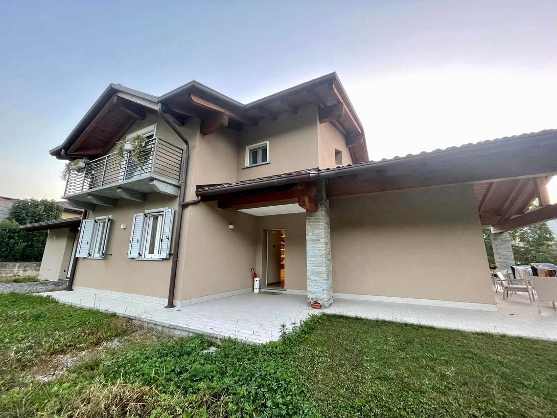 Casa beige a due piani con patio coperto e prato verde sotto un cielo luminoso