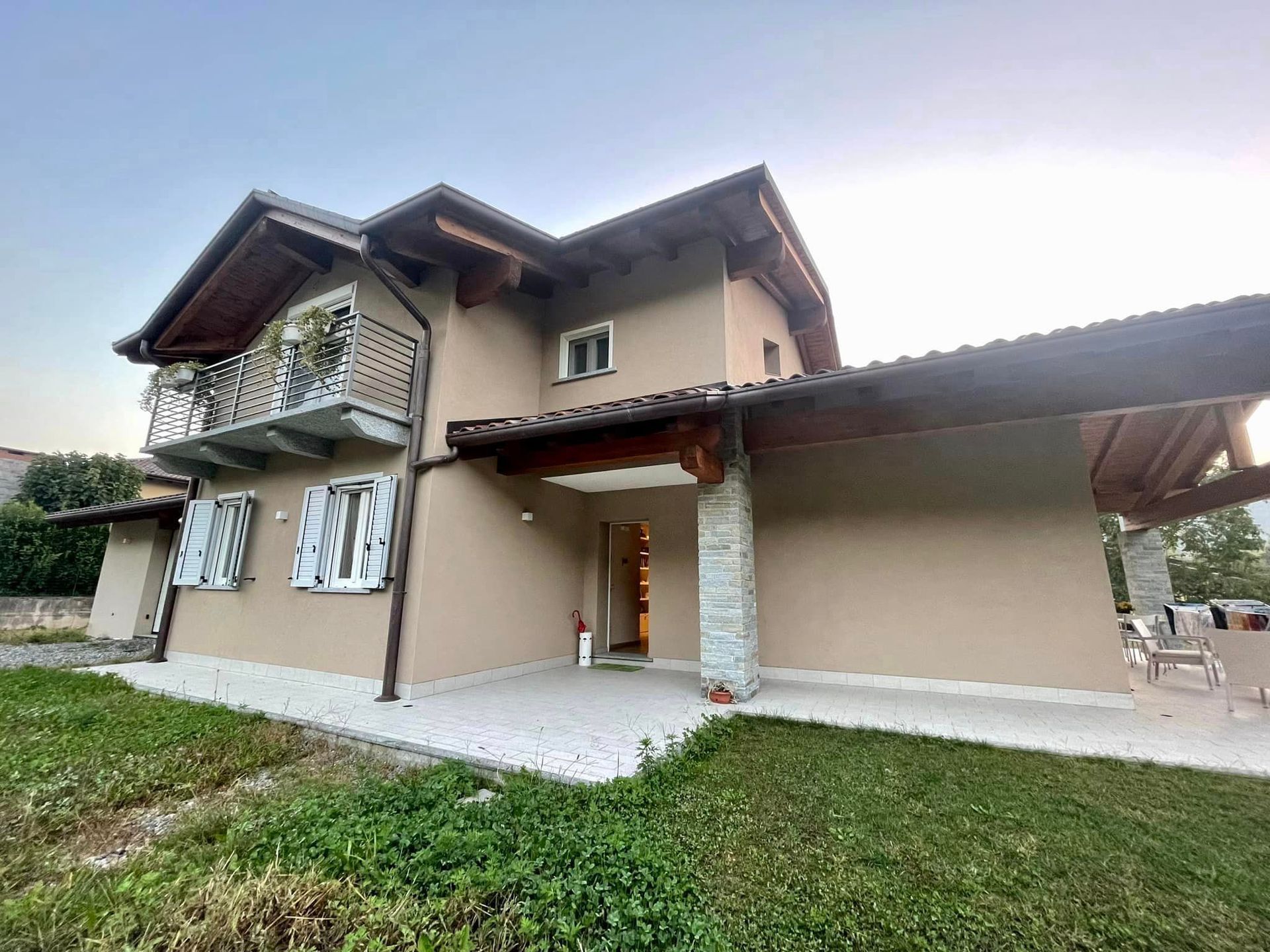 Casa beige a due piani con patio coperto e prato verde sotto un cielo luminoso