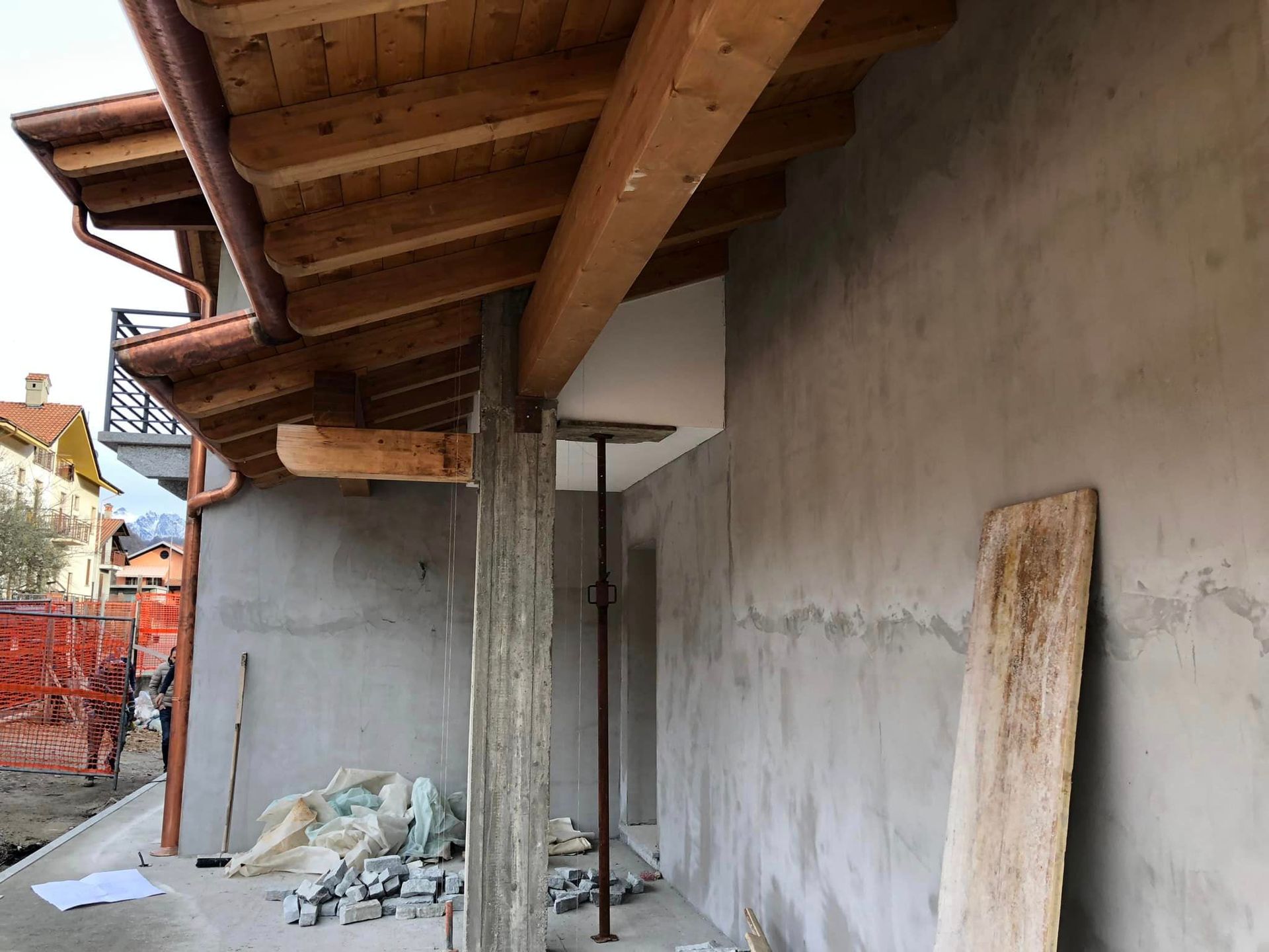 Cantiere edile con muro in stucco non rifinito, tettoia in legno e detriti a terra.