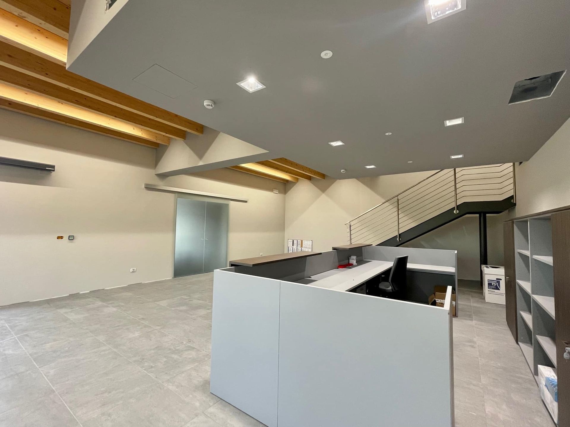 Interno di un moderno ufficio vuoto con pavimenti grigi, pareti bianche, dettagli in legno sul soffitto e una scala in vetro.