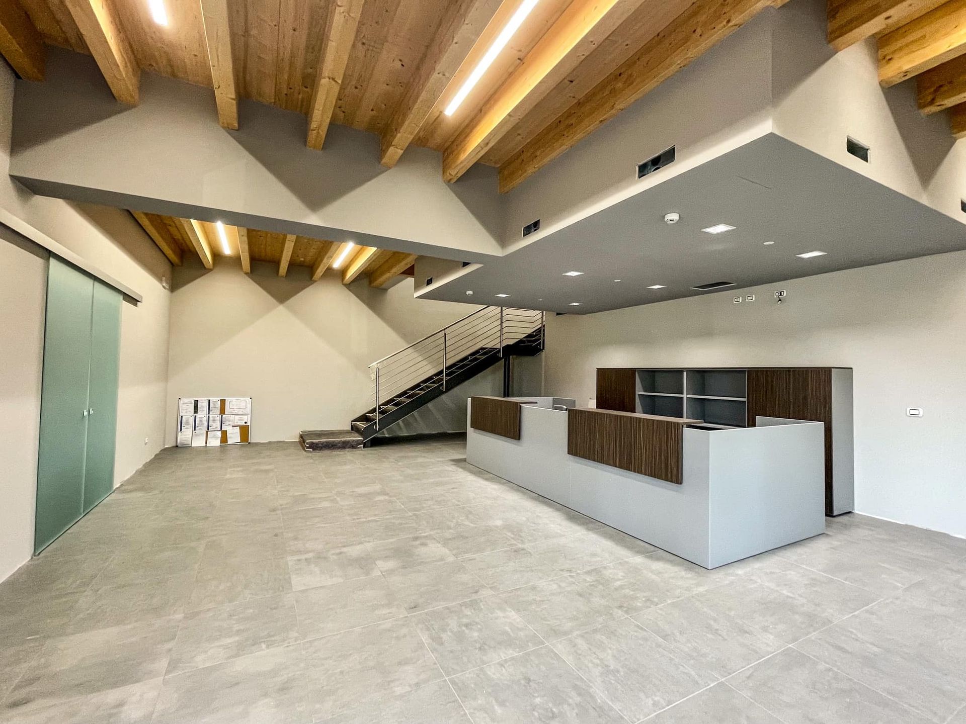 Moderna hall per uffici con travi in ​​legno a vista, scala a mezzanino e reception.