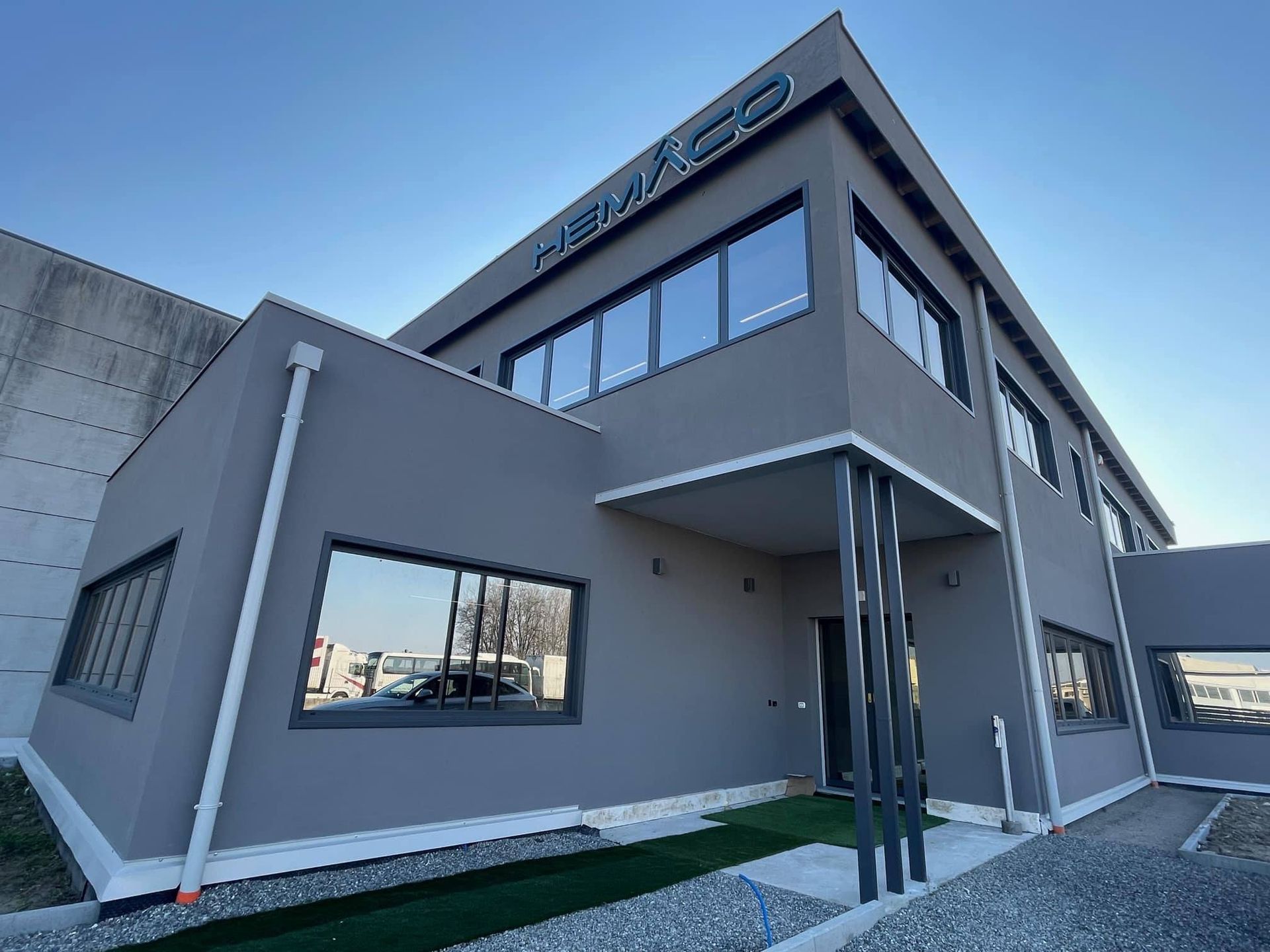 Moderno edificio per uffici di colore grigio con ampie finestre e ingresso coperto, visto da un'angolazione particolare.
