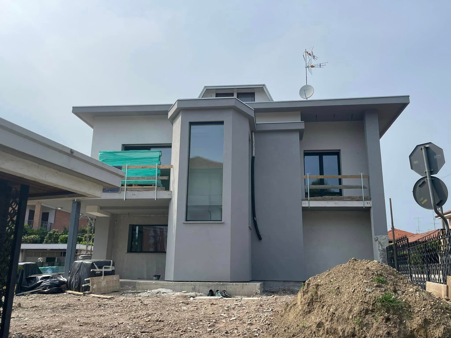 Casa moderna a due piani di colore grigio, in costruzione, con impalcature e cumulo di terra davanti.