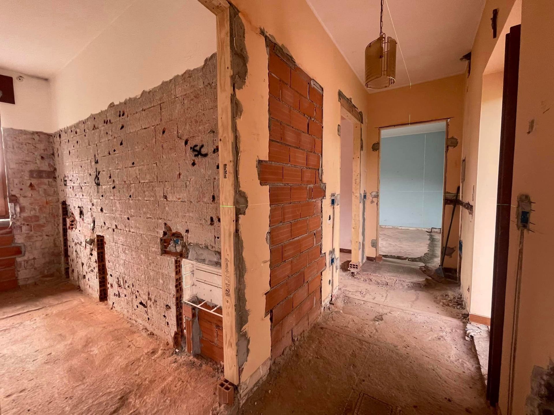 Corridoio parzialmente ristrutturato con pareti in mattoni a vista, residui di intonaco e porte aperte in fase di ristrutturazione