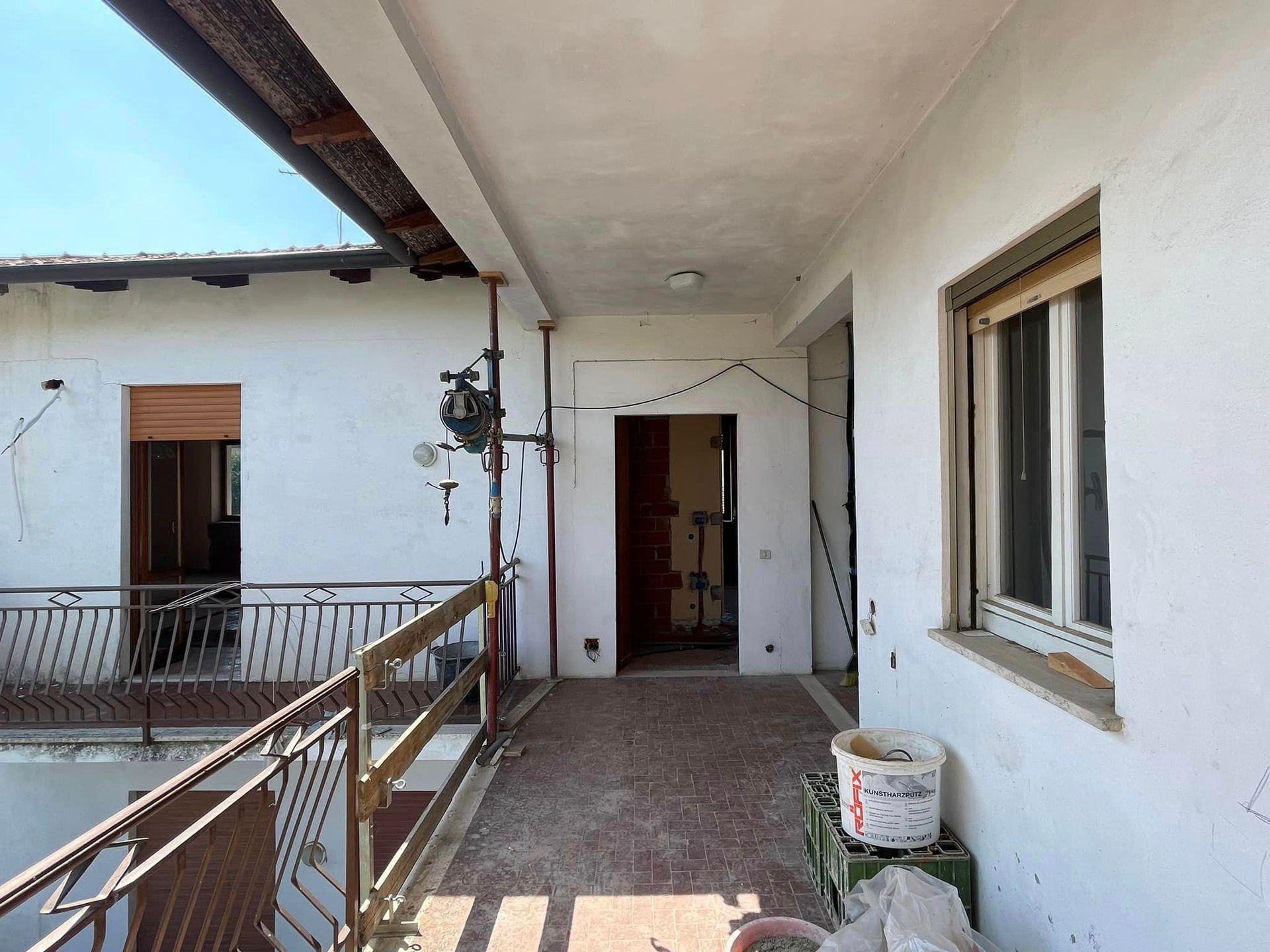 Stretto corridoio esterno con pareti bianche, ringhiere e porte aperte sul portico di un edificio residenziale.
