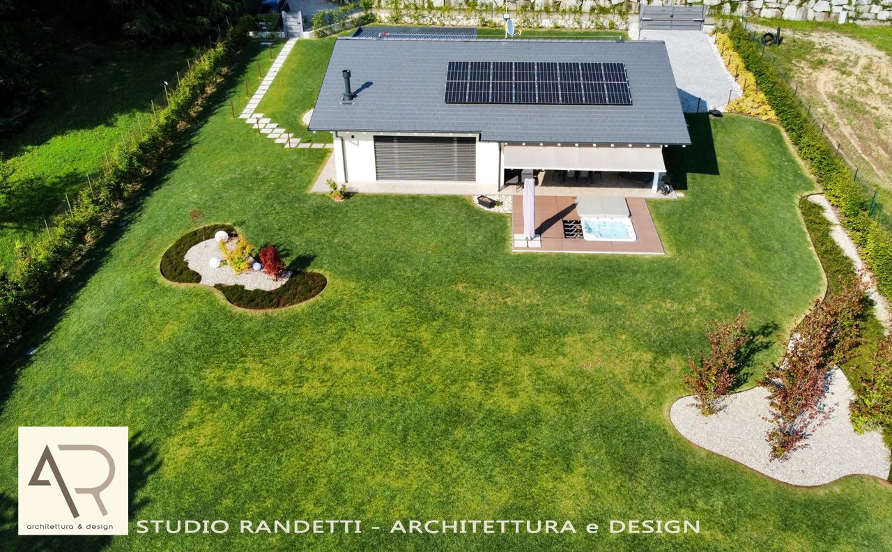 Veduta aerea di una casa moderna con pannelli solari, un prato verde e un piccolo laghetto in giardino.