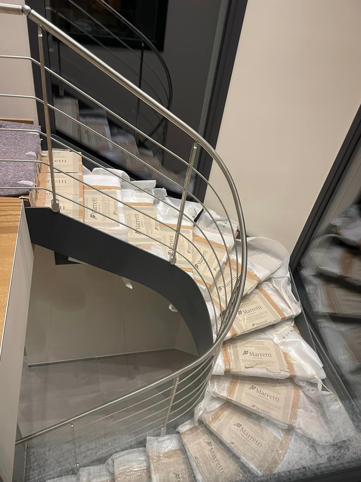 Scala curva in marmo con ringhiera in metallo nero in un interno moderno.