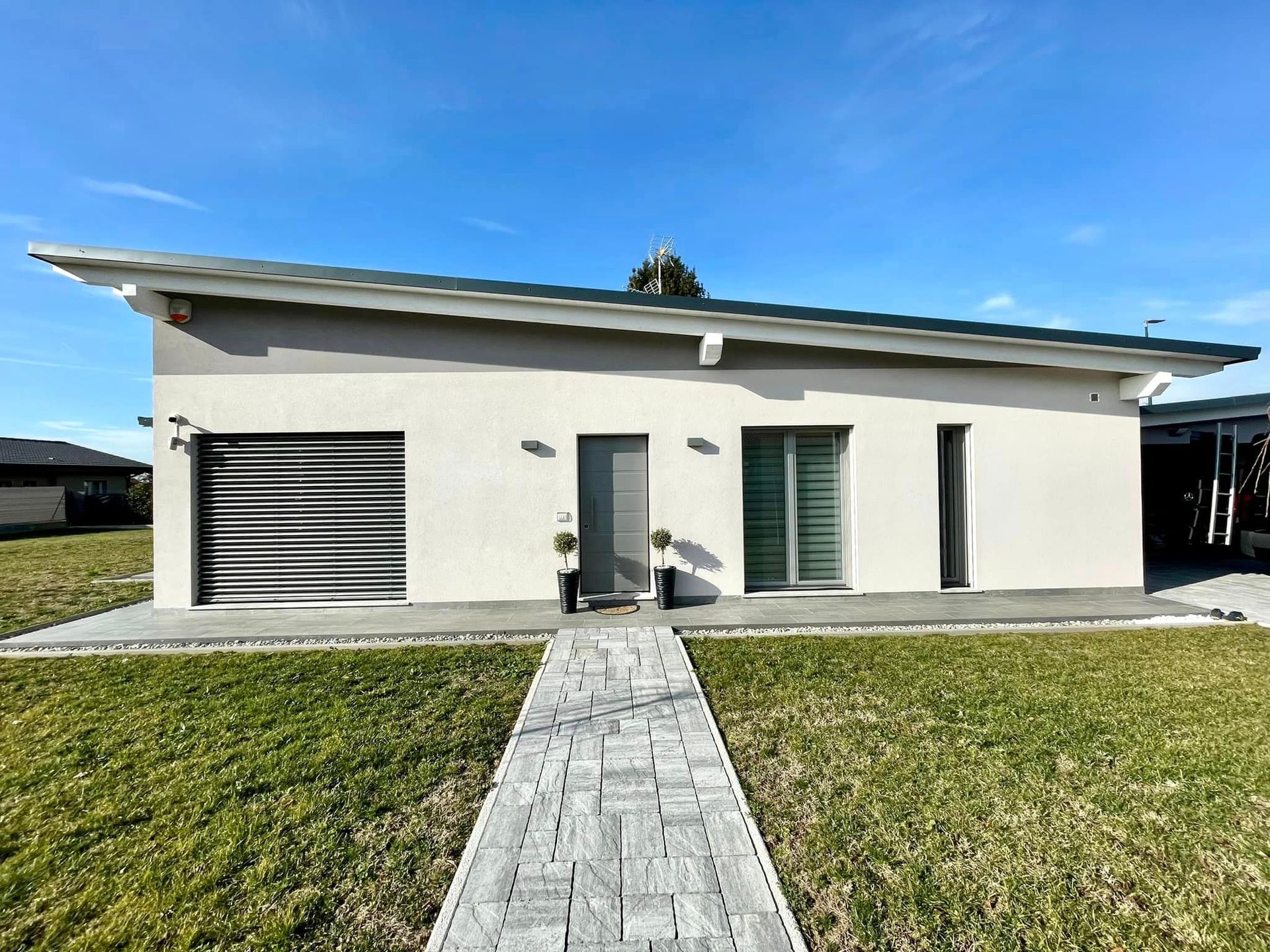 Casa moderna bianca a un solo piano con vialetto d'ingresso e giardino erboso sotto un cielo azzurro