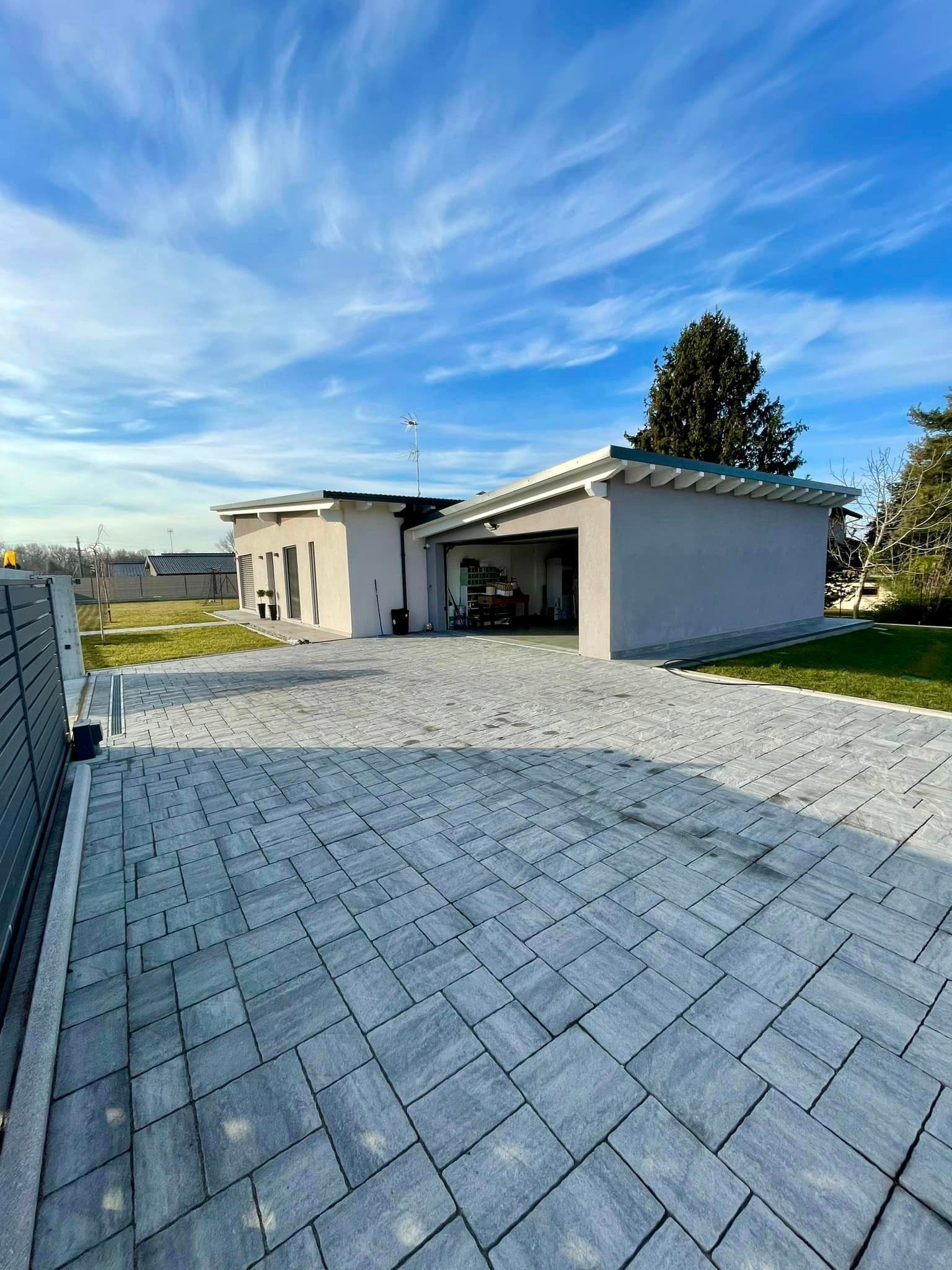 Casa moderna con un ampio vialetto pavimentato sotto un cielo azzurro