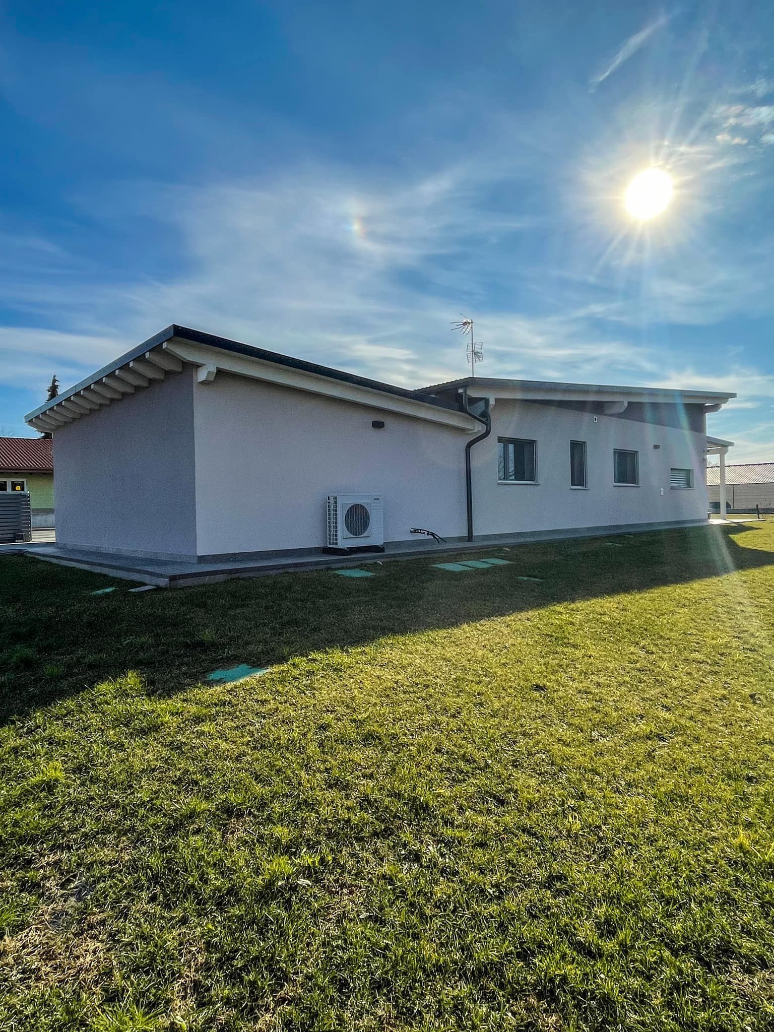 Casa bianca con tetto di tegole su un pendio erboso sotto un cielo azzurro brillante e un bagliore di sole