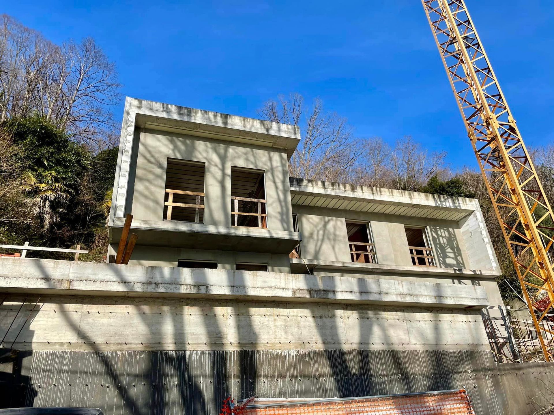 Cantiere edile con muri di cemento e una gru sullo sfondo di un cielo azzurro limpido.