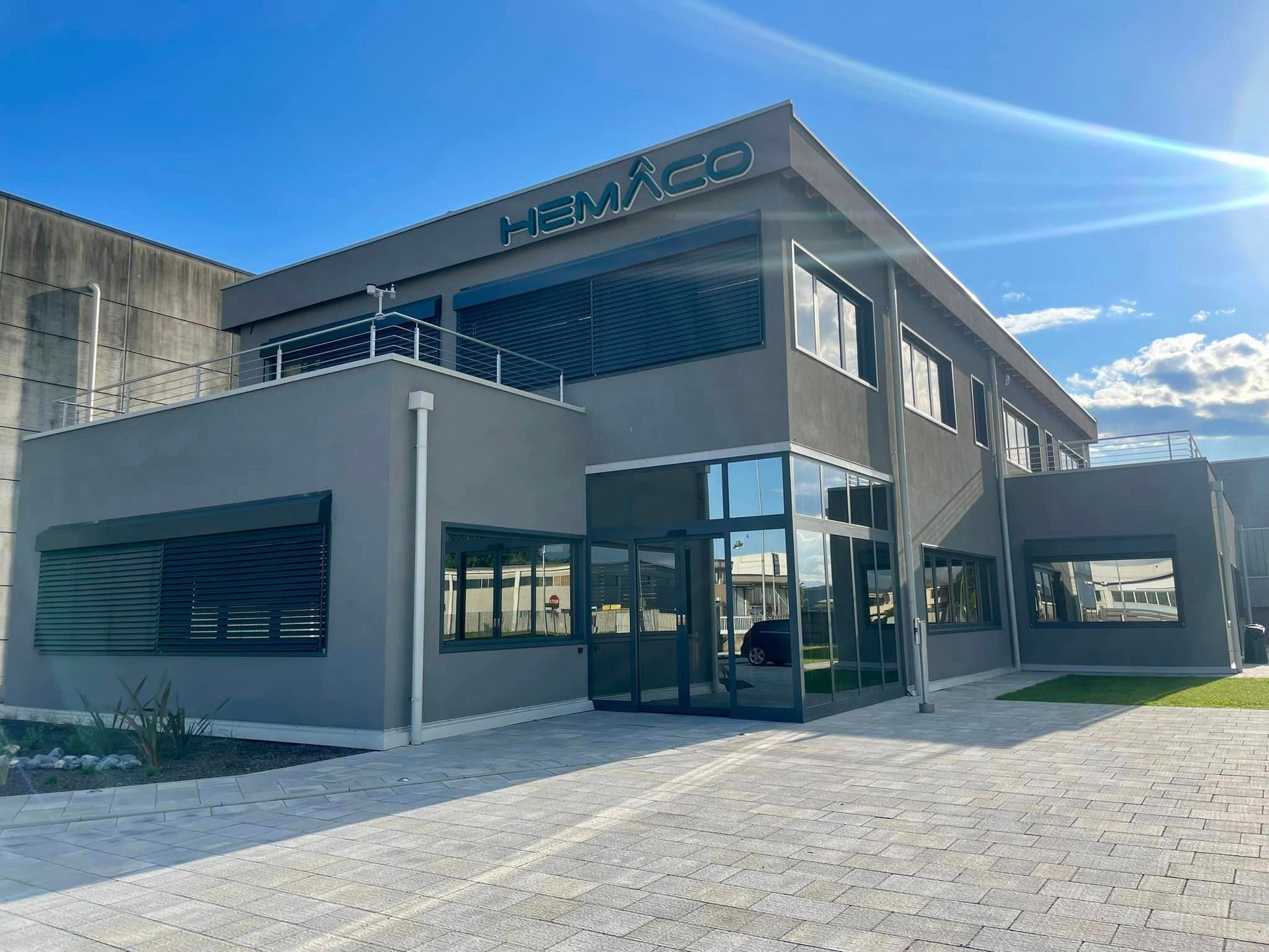 Moderno edificio per uffici a due piani con ingresso in vetro e facciata esterna in cemento, sotto un cielo azzurro e soleggiato.