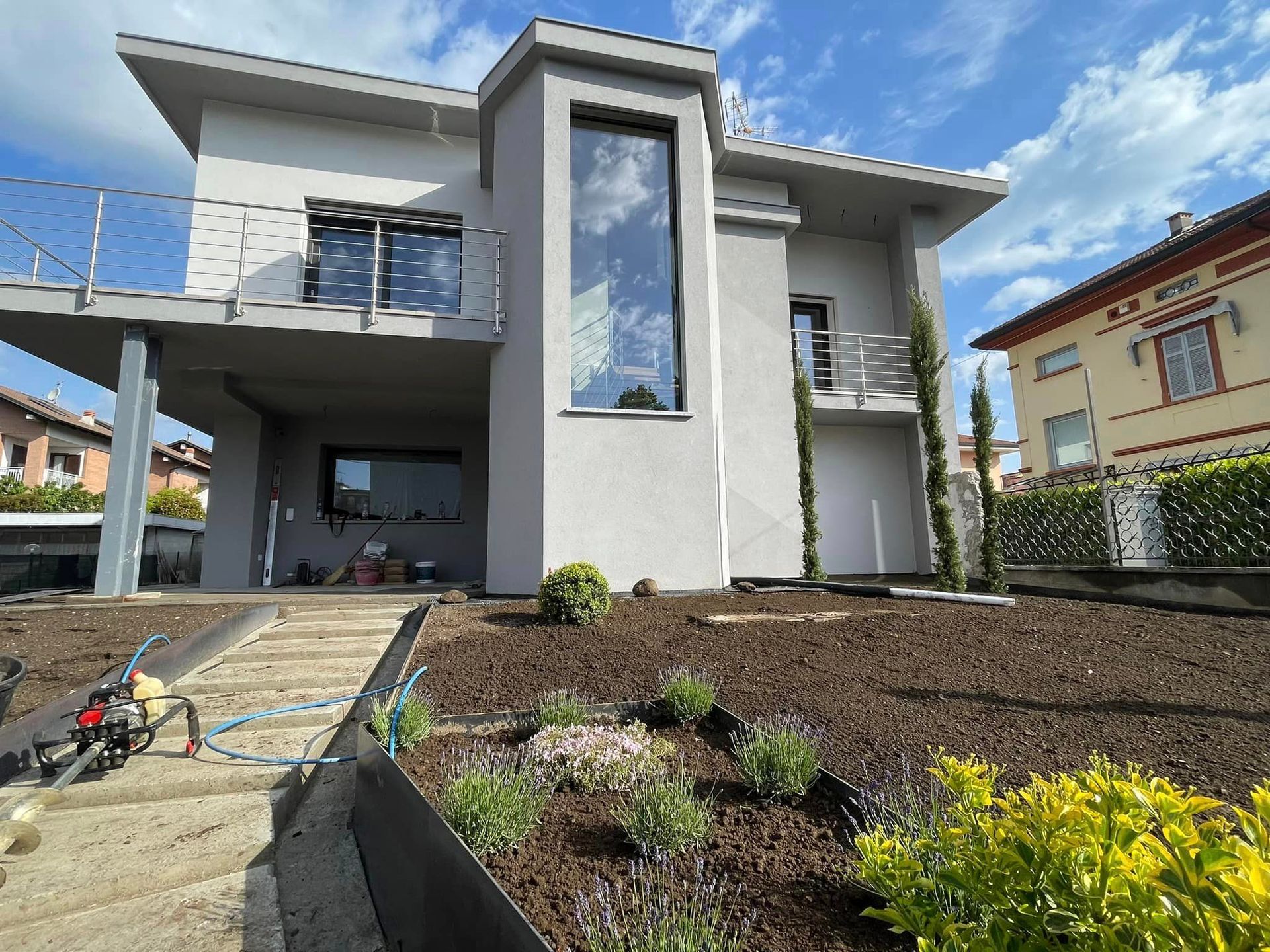 Casa moderna a due piani con facciata grigia, ampie finestre, vialetto d'accesso e giardino anteriore curato sotto un cielo azzurro.