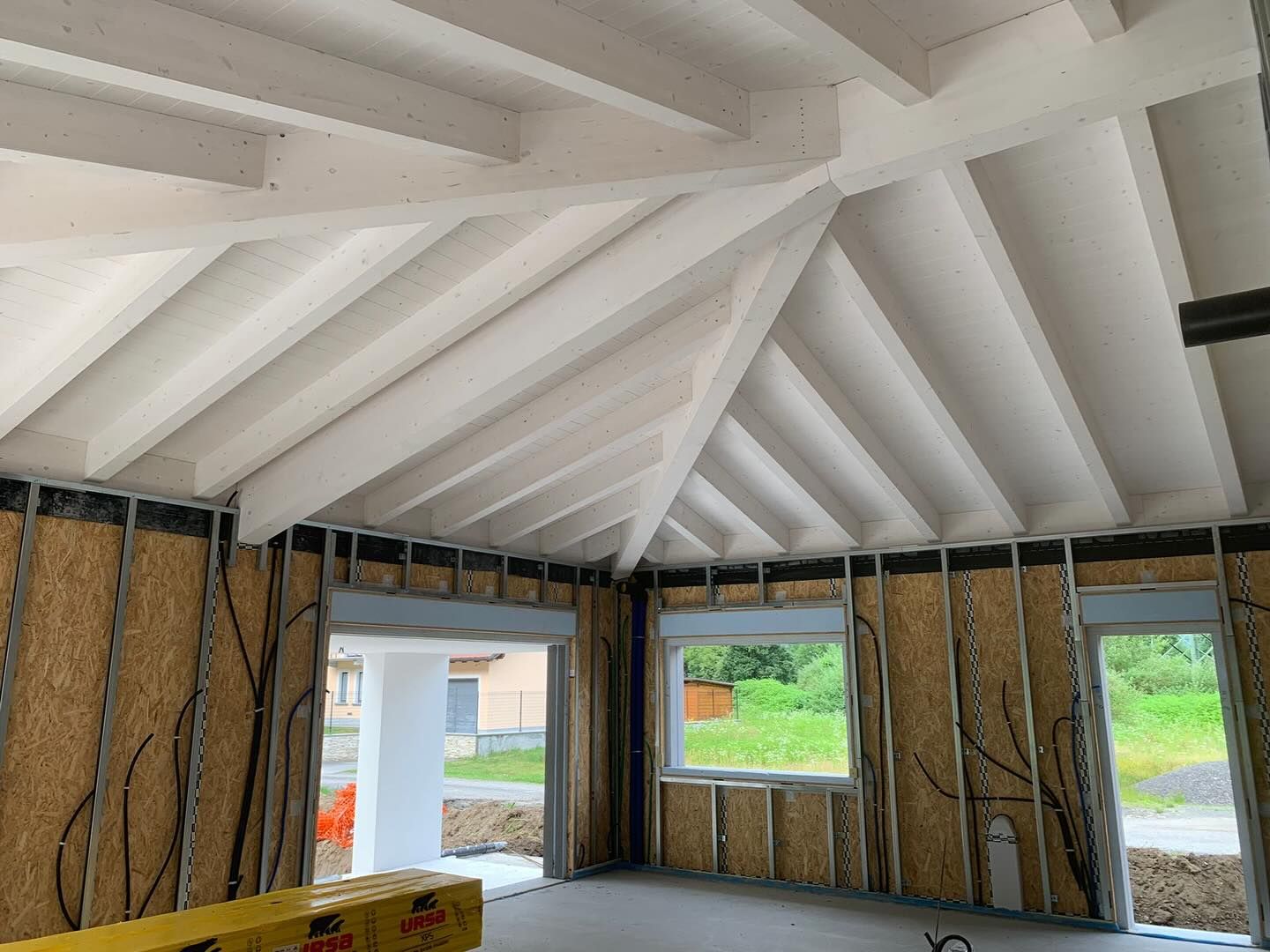 Stanza parzialmente rifinita con pareti isolate a vista e soffitto a volta bianco, con finestre e porta che si aprono verso l'esterno.