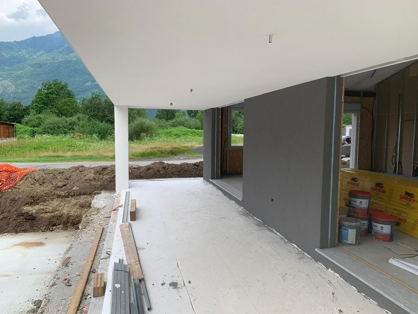 Veranda di una casa moderna parzialmente finita con pareti grigie, tettoia bianca e materiali edili accatastati all'interno.