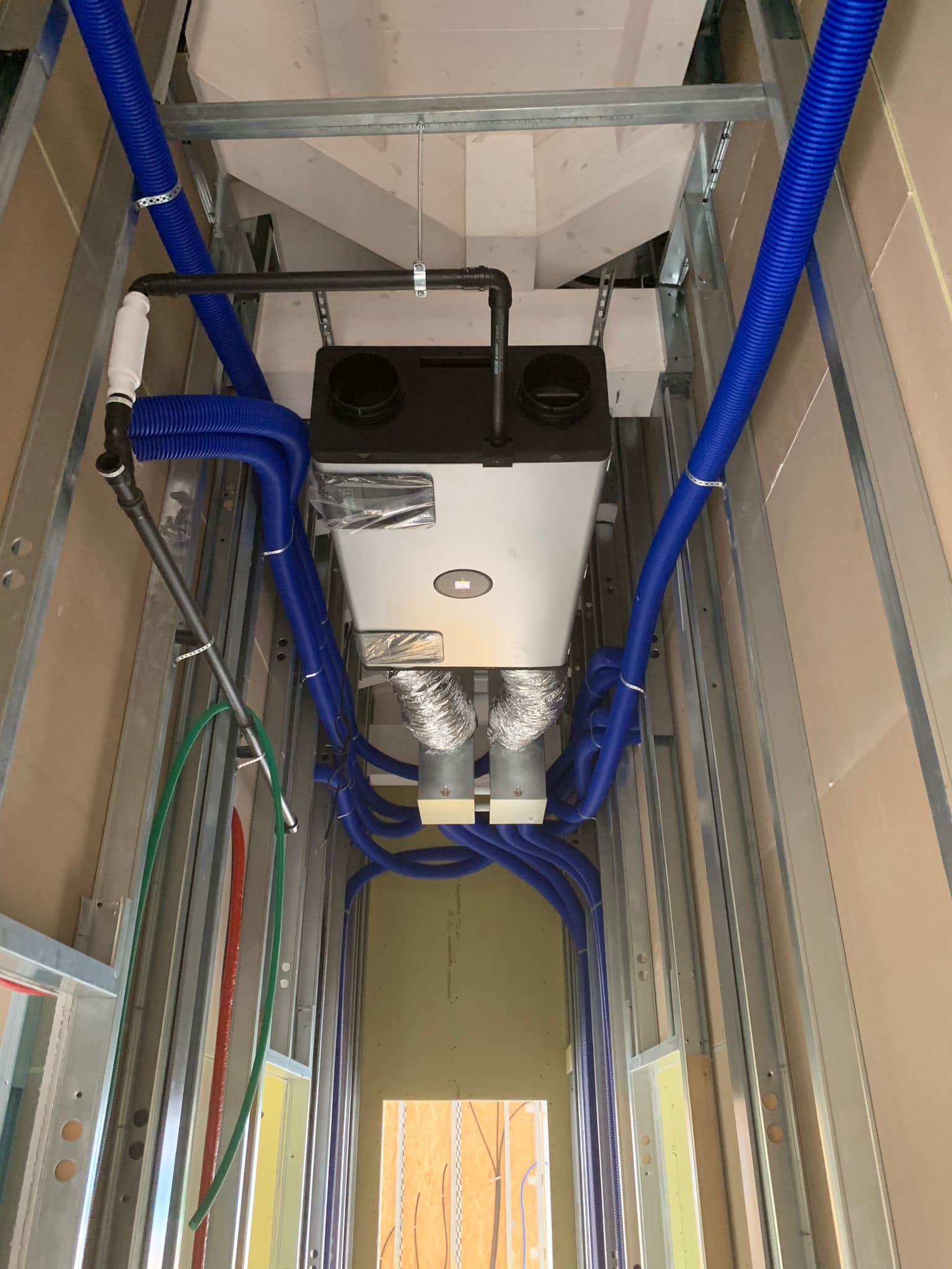 Unità di ventilazione a soffitto con condotti isolati blu all'interno di uno stretto vano tecnico.