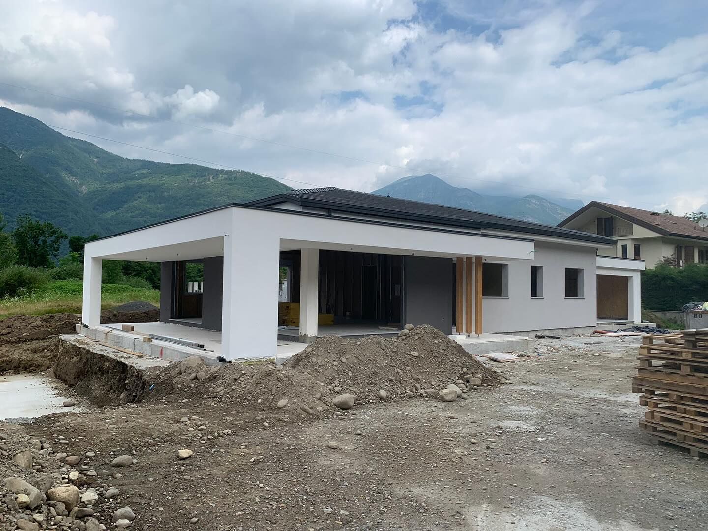 Casa moderna bianca in costruzione con montagne e cielo nuvoloso sullo sfondo.