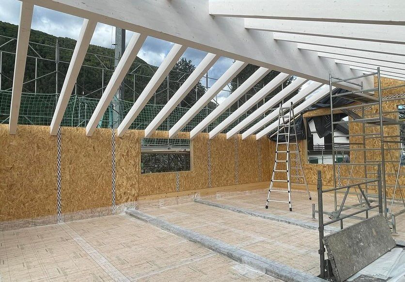 Stanza parzialmente costruita con travi a vista, scala, impalcature e pareti in compensato in fase di realizzazione.