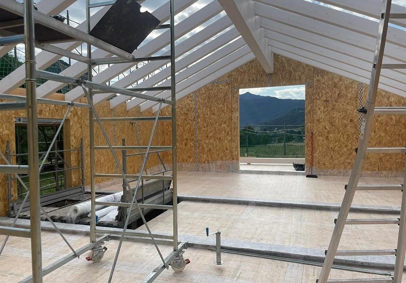 Interno di un edificio in costruzione con impalcature, pareti in legno a vista e vista sulle montagne attraverso l'apertura.
