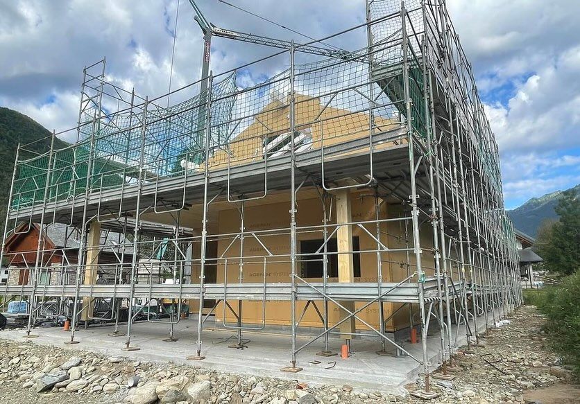 Casa in costruzione con impalcature verdi e pareti color beige sotto un cielo nuvoloso
