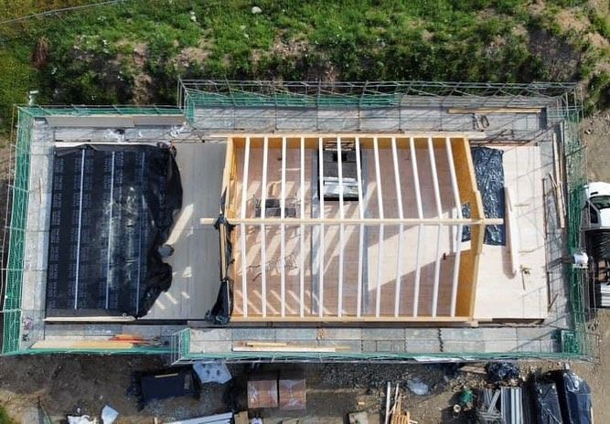 Vista dall'alto del tetto di una casa in costruzione, con la struttura in legno a vista e una sezione coperta da un telone nero.