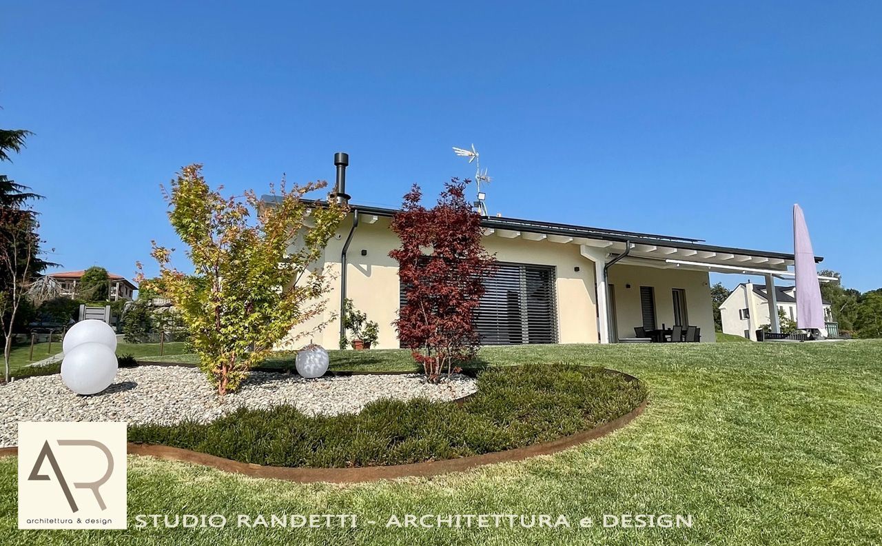 Casa moderna a un solo piano con prato curato, arbusti fioriti e un cielo azzurro limpido.