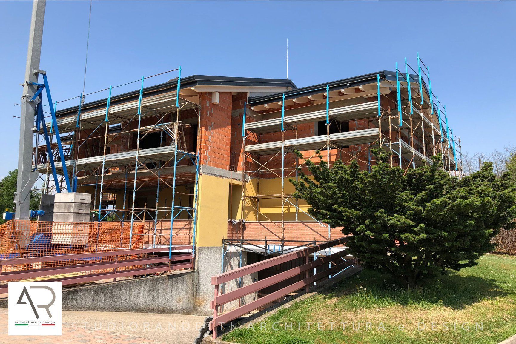 Edificio in mattoni parzialmente ristrutturato con impalcature e rete di sicurezza blu sotto un cielo sereno.