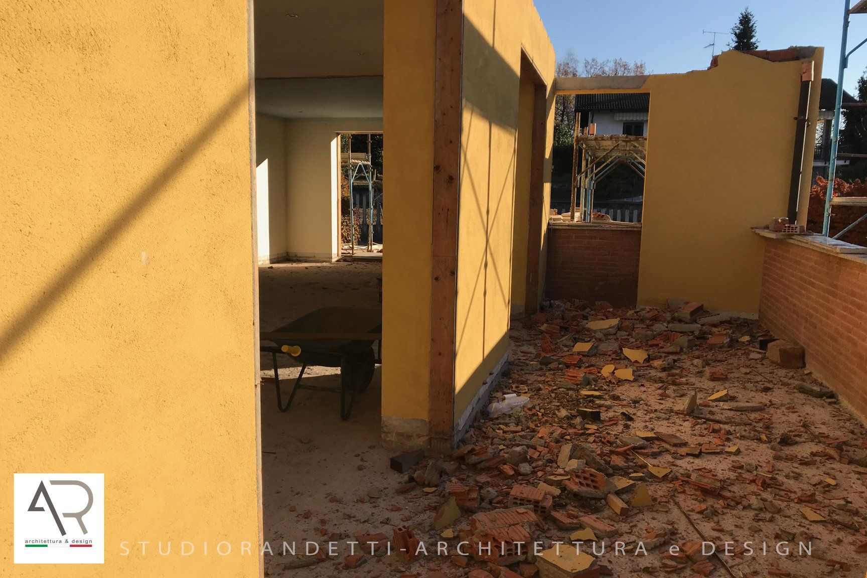 Patio giallo con pavimento piastrellato, stretto passaggio e una sedia vicino a una porta aperta.