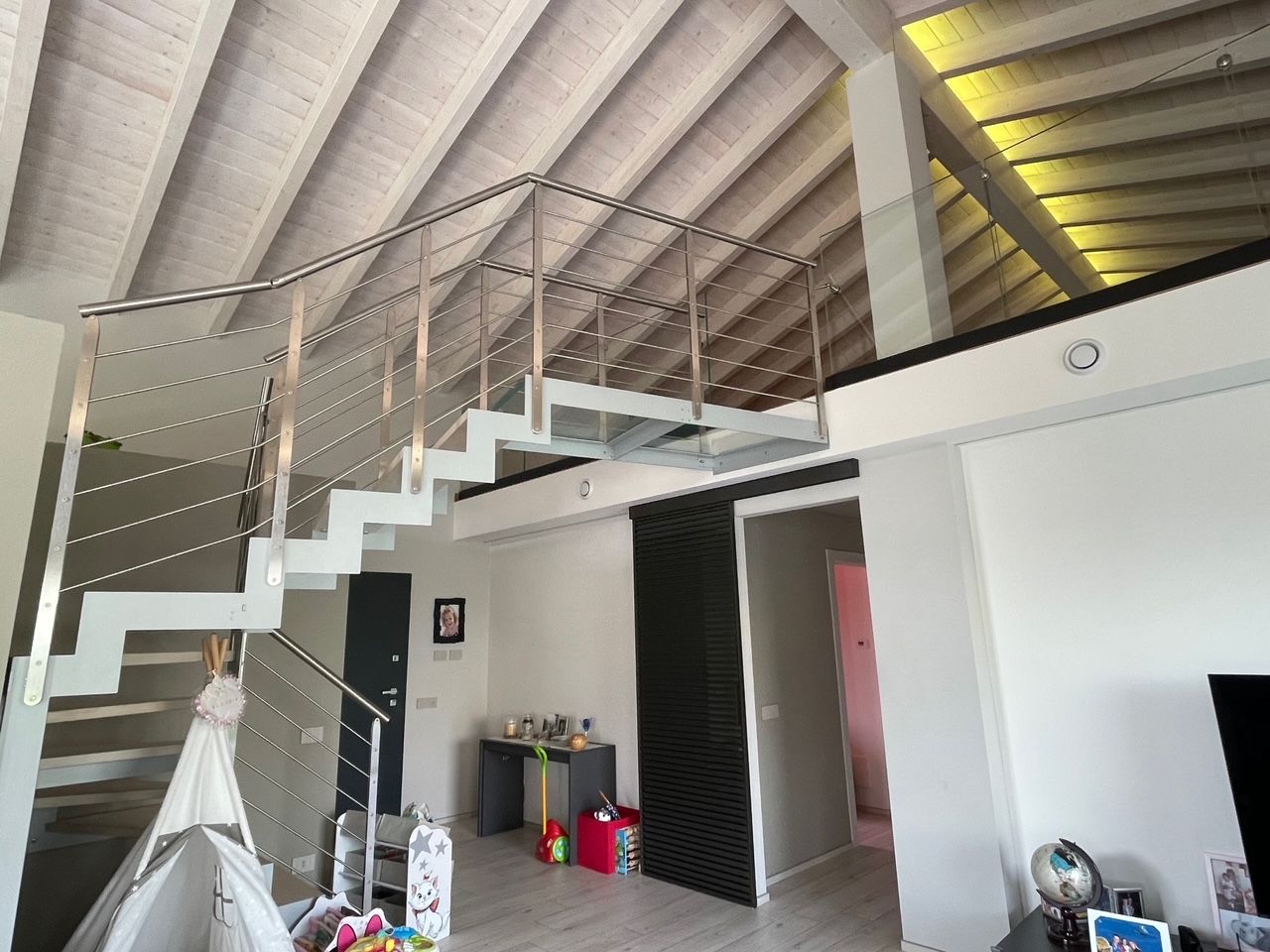 Interno di un loft con scala bianca, soffitto alto a volta e porta aperta su una piccola stanza.
