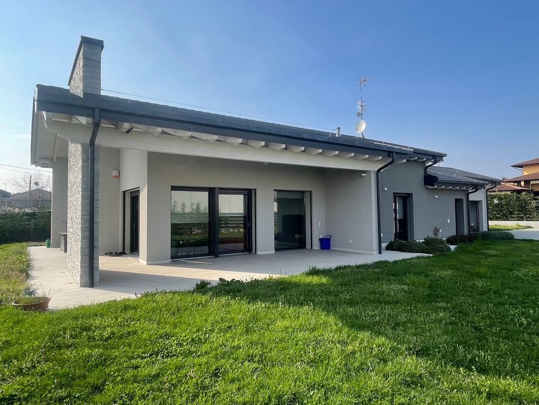 Casa moderna a un solo piano con tetto grigio, pareti bianche, porte finestre e giardino erboso.