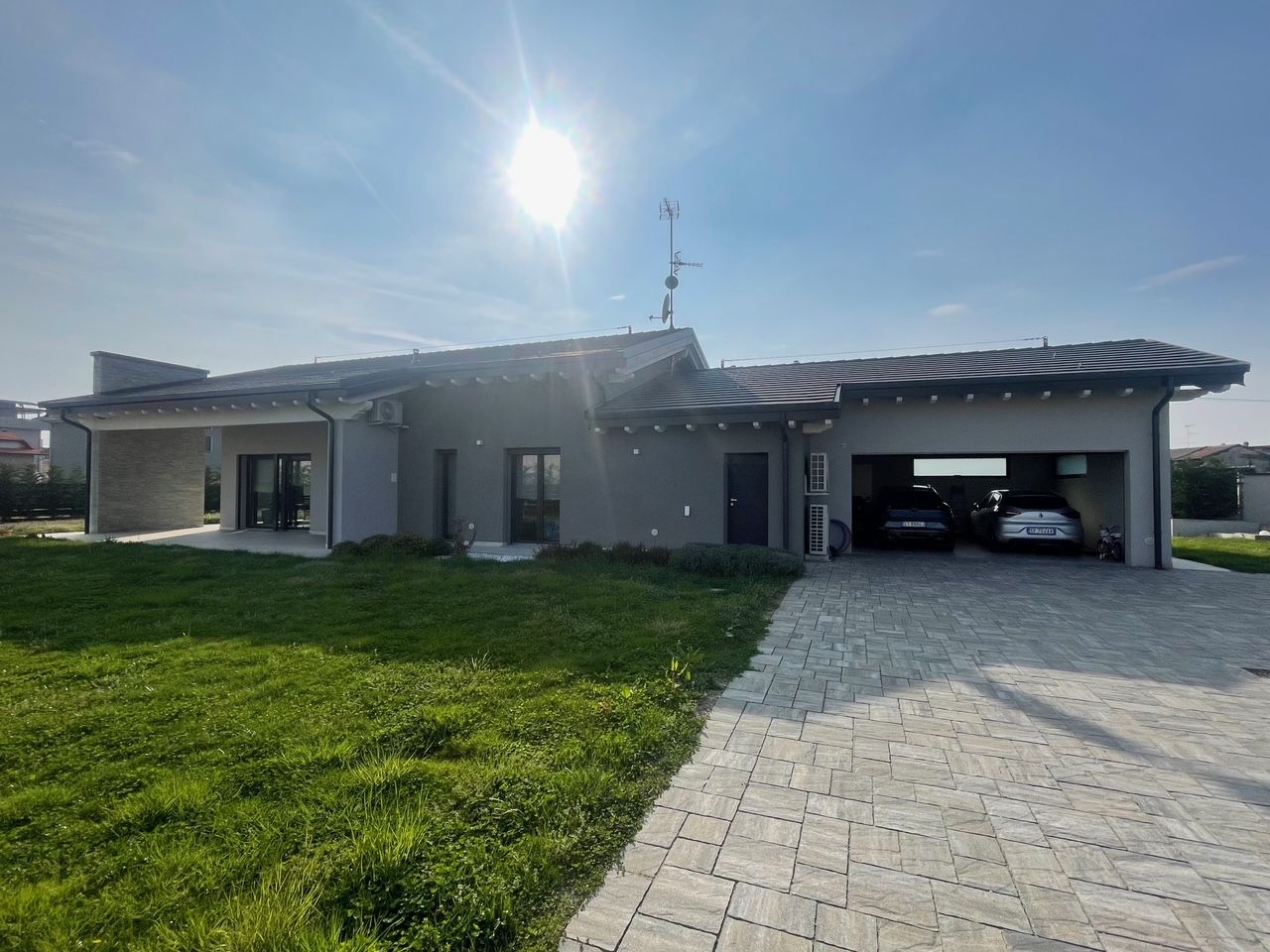 Casa moderna a un solo piano con vialetto pavimentato, prato verde e garage aperto sotto un cielo luminoso