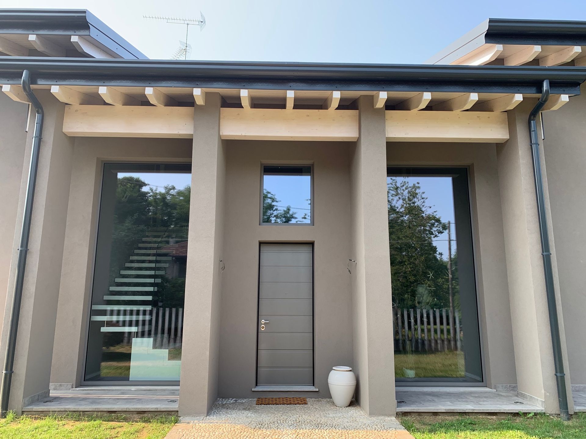 Ingresso di una casa moderna con porta grigia, finestre alte e colonne beige.
