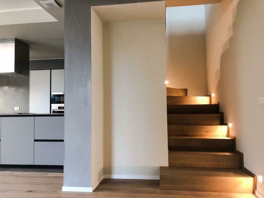 Interni moderni con scala in legno e piccolo pianerottolo illuminato accanto alla zona cucina.