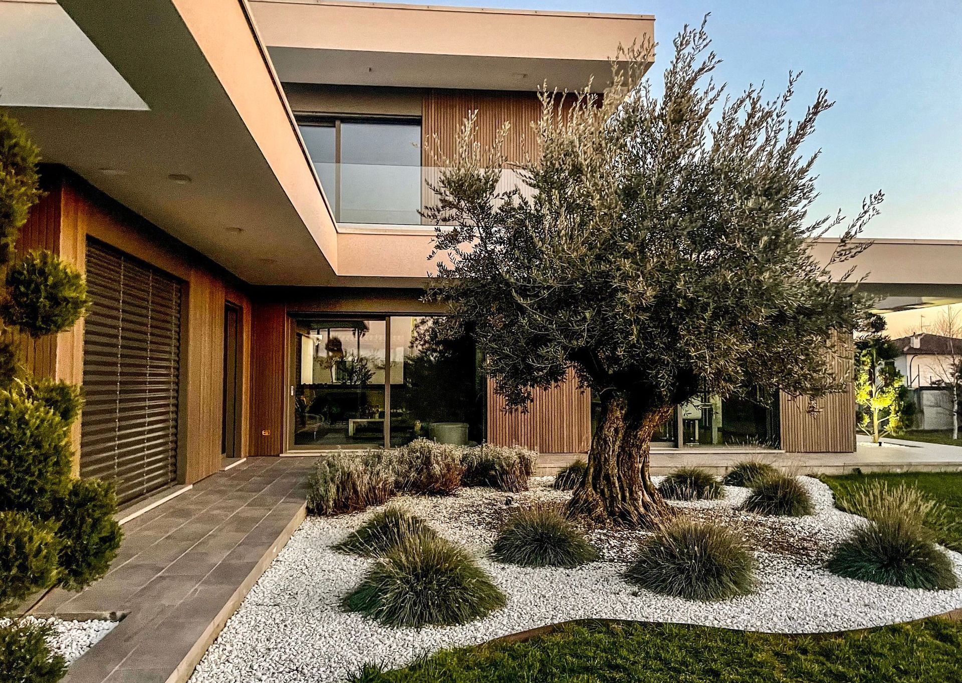 Esterno di una casa moderna con rivestimento in legno, un grande albero e un giardino anteriore con ghiaia.
