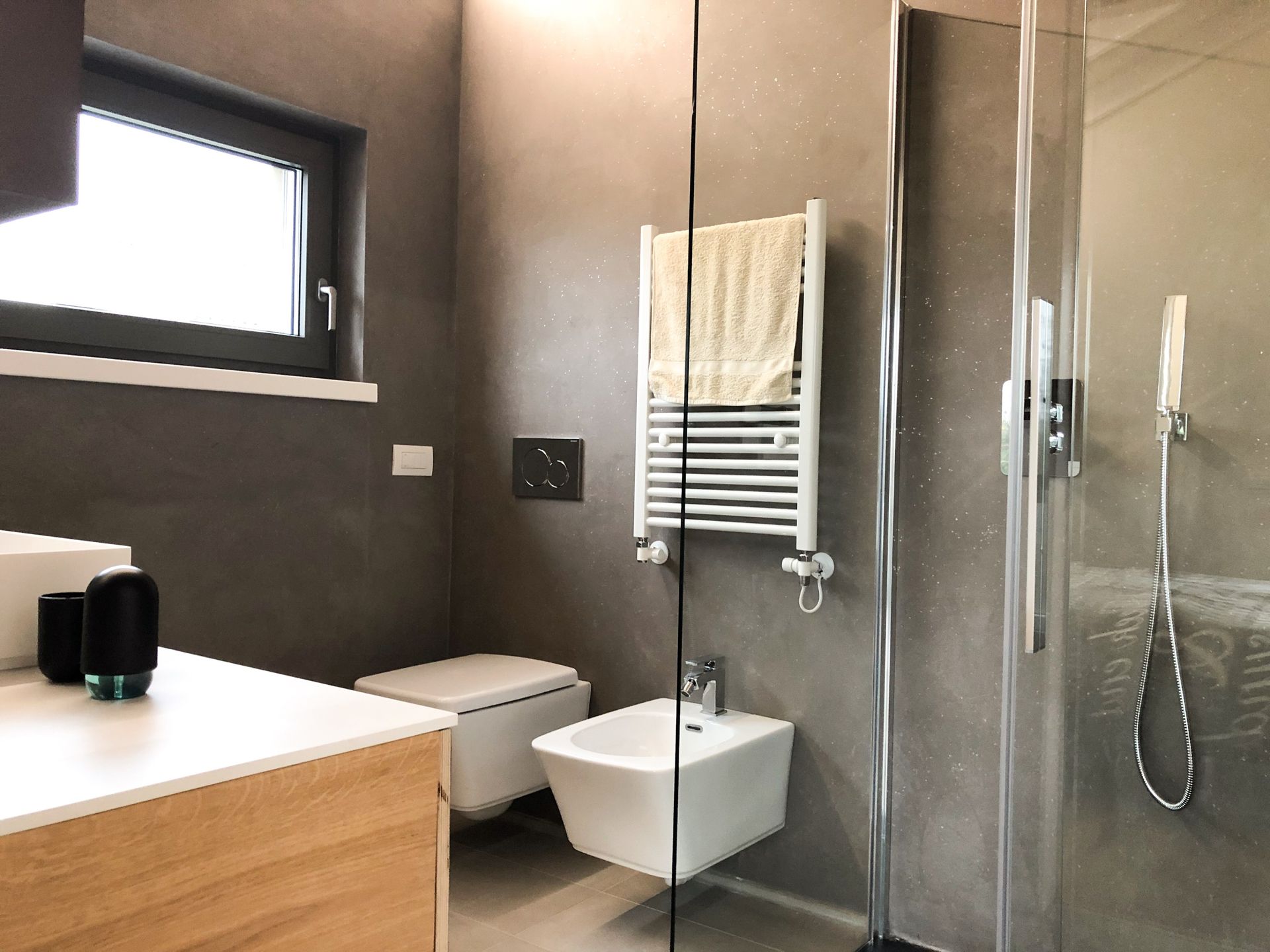 Bagno moderno con cabina doccia, lavabo a parete, WC e portasciugamani su pareti rivestite con piastrelle grigie.